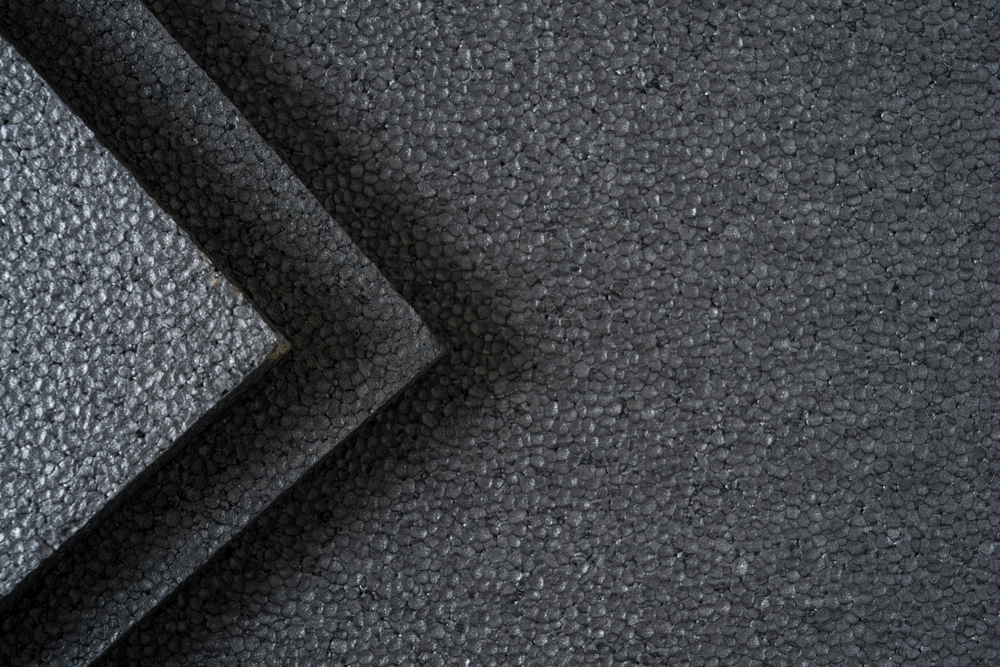 Close-up of dark gray foam packaging material with a textured, beaded surface, showing overlapping foam pieces arranged diagonally.